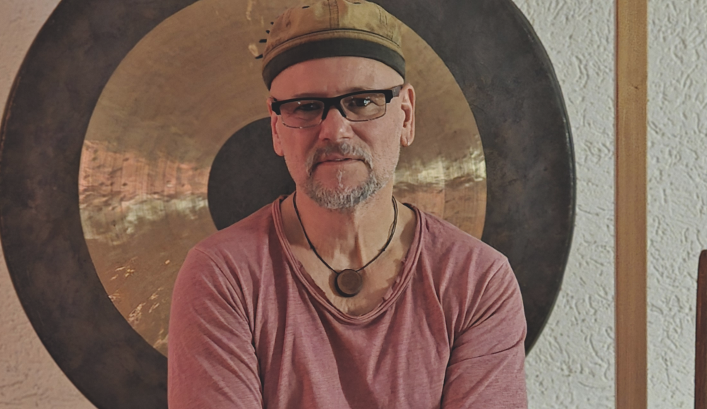 oey Krüger vor einem großen Gong – Klangtherapeut während einer Klangreise in ruhiger, achtsamer Atmosphäre